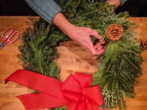 hands adding pine cones into wreath