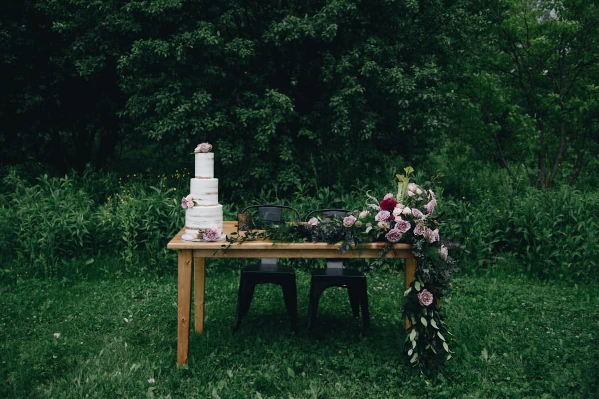 farm table decorated with small wedding cake and sprawling floral arrangement