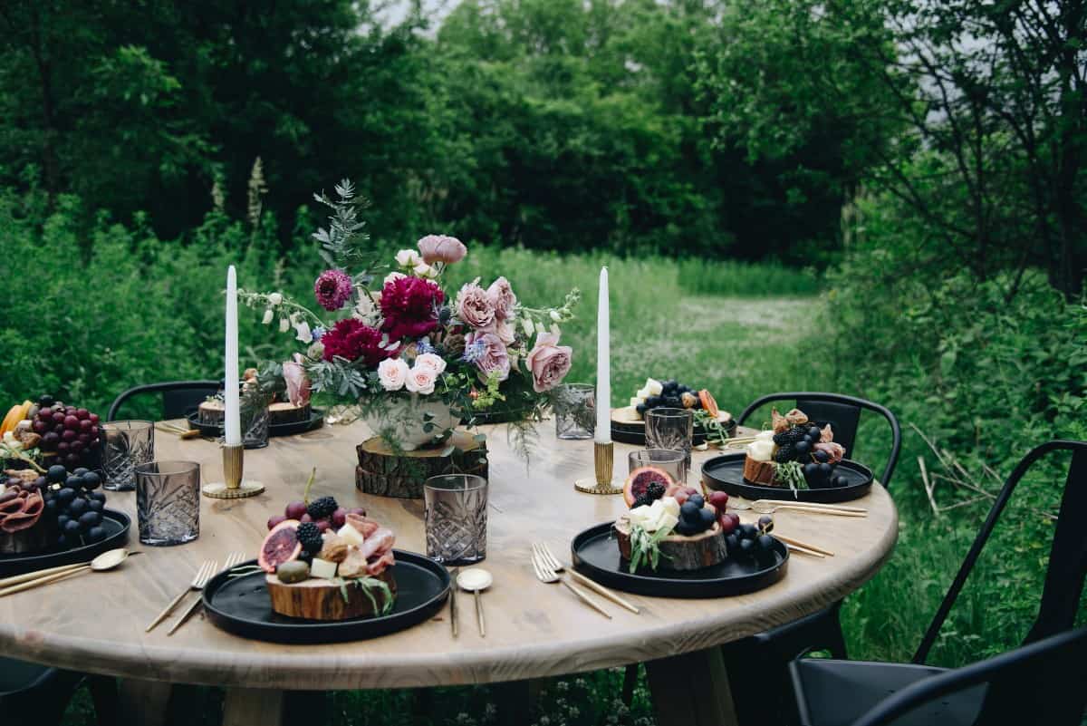 round guest table in a meadow decorated with floral centerpiece and individual charcuterie plates.