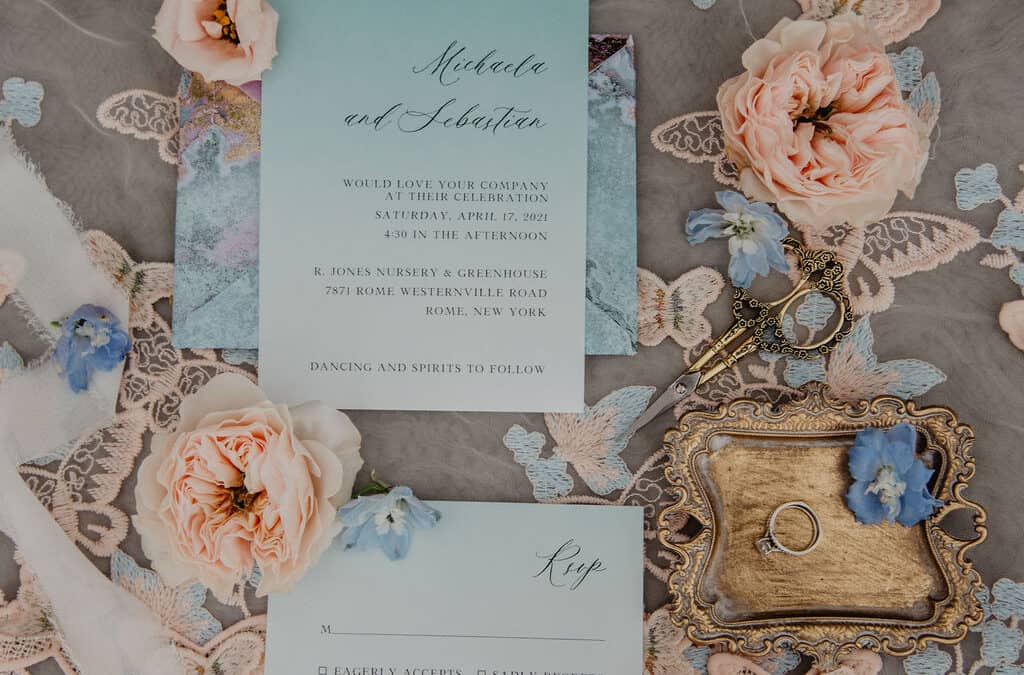 flat lay with peach roses, delphinium florets and wedding invitation